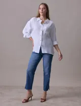 Camisa blanca de algodón con textura arrugada, cuello con solapa, abertura central con botones y bolsillo aplicado en el pecho. Mangas largas con largo regulable mediante presilla y botón.