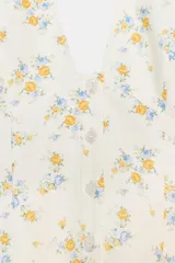 Vestido corto blanco con estampado floral en tonos amarillo y azul. Diseño con cuello halter, escote pronunciado en pico y cierre frontal de botones.