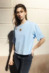 Remera blanca de algodón con cuello redondo y mangas cortas. Presenta un bordado del sol de la bandera uruguaya en el pecho.