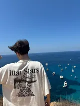 Remera celeste con estampa de paisaje costero y texto "Ittai Stars" y nombres de ciudades.
