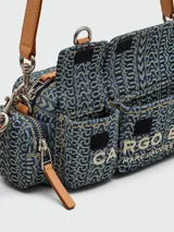 Bolso bandolera Marc Jacobs modelo The Cargo Monogram Denim, con estampado del logo de la marca en azul y verde. Tiene correa de cuero marrón, cierre superior con cremallera, dos bolsillos frontales con hebilla y herrajes dorados.