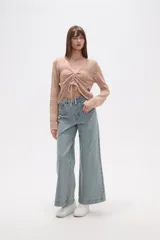 Sweater de poliéster color beige, con cuello en V, manga larga y frunces ajustables en el frente. Presenta un diseño de tejido calado.