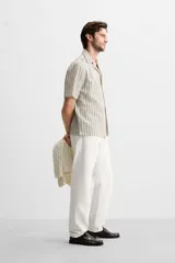 Camisa de hombre relaxed fit confeccionada en tejido de algodón a rayas verticales blancas y negras. Tiene cuello bowling, manga corta, bajo con aberturas laterales y cierre frontal de botonadura.