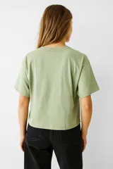 Remera corta color crudo de algodón, con cuello redondo y mangas cortas. Presenta tres lazos bordados en el frente.