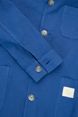 Chaqueta azul con textura seersucker, cuello con solapa, cierre con botones, bolsillo en el pecho y dos bolsillos de parche redondeados.