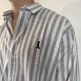 Camisa de manga larga a rayas verticales grises y blancas, con cuello clásico y cierre frontal con botones.