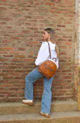 Mochila pequeña de cuero color camel, con base marrón, laterales color crema y cierre superior con cremallera.