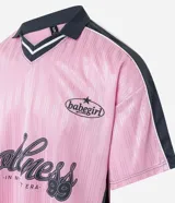 Remera rosa con cuello polo gris y rayas verticales. Estampado frontal con la palabra "gobline" en letras cursivas y la frase "in my best era". Diseño oversized con mangas cortas y recortes laterales en color negro.