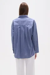 Camisa de algodón blanca de corte holgado, con cuello camisa y manga larga. Presenta un estampado de finas rayas verticales negras y un bolsillo frontal con rayas horizontales.