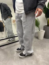 Pantalón de jogging gris de algodón, corte oversize, con costuras o cortes decorativos en la parte delantera de las piernas. Presenta un pequeño bordado en la zona del bolsillo.