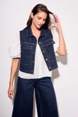 Chaleco de jean azul oscuro con cuello, bolsillos frontales y cierre con botones dorados. Corte al cuerpo.