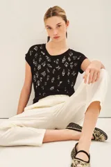 Remera negra de viscosa con calce suelto, escote redondo, manga corta y estampado frontal con bordado de lentejuelas doradas.