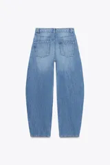 Pantalón de jean celeste de tiro medio, corte amplio tipo globo, con bolsillos delanteros y traseros, trabillas en la cintura, abertura lateral en el ruedo y cierre frontal con cremallera y botón.