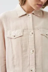 Chaqueta color beige melange de lino con pespuntes a contraste, cuello camisero, cierre frontal con botones, bolsillos de parche en el pecho y corte recto.
