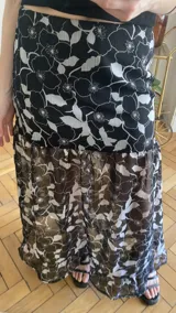 Falda larga de tela estampada con motivos florales en tonos marrones, negros y violetas. Tiene elástico en la cintura y corte acampanado.