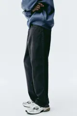 Jean negro de denim de algodón rígido, corte holgado de cadera a bajo con piernas redondeadas extraamplias y pliegues al tobillo. Cintura clásica con cierre y tiro bajo.