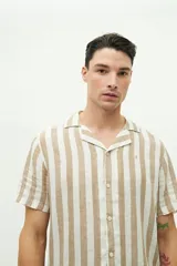 Camisa de manga corta confeccionada en lino y algodón a rayas verticales en tonos blanco, gris y beige. Tiene cuello tipo cubano, corte regular y logo bordado en el pecho.