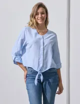 Blusa de algodón a rayas verticales finas en tonos blanco y lila, con escote en V, abertura frontal con botones y mangas largas regulables con presilla y botón. El ruedo termina anudado al frente.