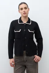 Chaqueta de tejido color terracota/lacre, con cuello y bordes de bolsillo en blanco con textura de punto. Posee cierre frontal de botones y manga larga.