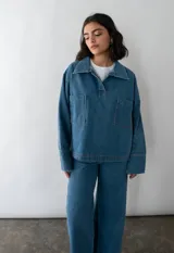 Camisa celeste de denim con cuello clásico, mangas largas con puños abotonados, cierre frontal con botones a presión y dos bolsillos de parche en el pecho.