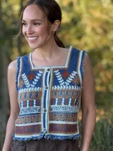 Chaleco corto de denim azul con bordado artesanal en tonos naranja, blanco y marrón. Tiene escote cuadrado, cierre de botones y terminaciones desflecadas.