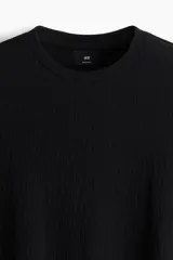 Remera negra de punto texturizado, corte regular, cuello redondo y mangas cortas.