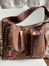 Cartera de cuero color chocolate con remaches metálicos, diseñada para uso cruzado o al hombro, con múltiples bolsillos.