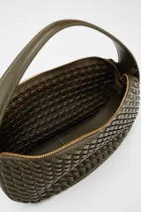 Bolso de mano color verde oliva con efecto trenzado. Tiene asa corta y correa larga extraíble. El cierre es con cremallera metálica.