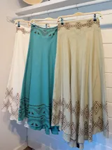 Pollera larga color celeste con estampado de guardas geométricas en color marrón en la cintura y el ruedo. Corte amplio y fluido.