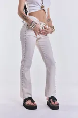 Pantalón jean color crudo, de corte recto y tiro medio, con tachas plateadas en los laterales. Sin lycra.