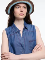 Camisa sin mangas en denim color celeste, confeccionada en 100% lyocell. De corte recto y largo medio, presenta cartera escondida en el frente y un bolsillo plaqué en el pecho. En la espalda, tiene botones decorativos alineados en abertura vertical y pespuntes a contratono.
