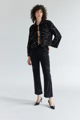 Pantalón de denim negro con tachas plateadas formando diseños geométricos.