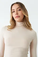 Polera color beige de corte crop, cuello alto y mangas largas.