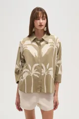 Camisa blanca con estampado de palmeras en color azul marino, de corte holgado, con cuello camisero, cierre frontal con botones y mangas 3/4 con puños anchos.