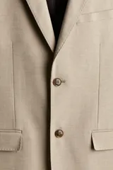 Blazer color beige de corte slim fit, con solapas de muesca finas, botonadura sencilla con cierre de dos botones, bolsillo superior, bolsillos delanteros con solapa, tres bolsillos interiores, botones decorativos en los puños y abertura atrás.