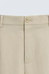 Pantalón de corte holgado (wide fit) en color beige, confeccionado en tejido con mezcla de lyocell. Presenta pliegues frontales en la cintura, bolsillos laterales y bolsillos traseros de doble vivo. Cuenta con cierre frontal de cremallera y botón.