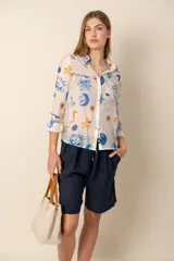 Camisa celeste con estampado de soles, lunas, flores y tortugas en tonos verdes, amarillos y naranjas.