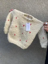 Sweater de lana merino color crema con pequeños corazones rojos bordados.