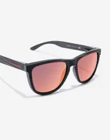 Gafas de sol unisex Hawkers edición limitada Alex Rins, con montura cuadrada negra con textura de fibra de carbono y lentes polarizadas color naranja.