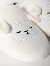 Pantufla blanca de textura peludita, con talón descubierto y diseño bordado en forma de animal, acolchada y con suela de 1,5 cm.