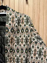 Chaqueta con estampado de arabescos en tonos marrones, beige y negro, con cuello mao, mangas largas y lazo para ajustar en la cintura.