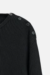 Sweater negro de punto con estructura de canalé, corte relaxed fit, cuello redondo y cierre de botones en el hombro.
