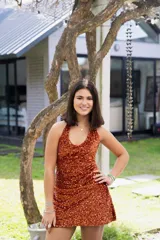 Vestido corto color naranja brillante con lentejuelas, escote halter y espalda descubierta.