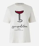 Remera de algodón color crema con cuello redondo y mangas cortas. Estampa frontal de una copa de Cosmopolitan y la inscripción "Cosmopolitan".