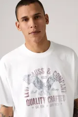 Remera blanca de corte holgado con estampado de águila y texto en tonos violeta y gris.