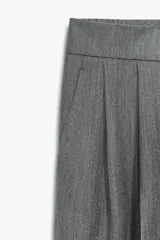 Pantalón color verde claro de tiro alto, con bolsillos delanteros, cintura elástica en la parte trasera y cierre frontal con cremallera y botones.