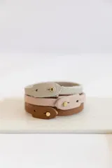 Set de cuatro pulseras finas de cuero en colores borgoña, rosa pálido, gris y verde oscuro. Cada pulsera tiene un cierre con botón metálico y algunas tienen palabras grabadas.
