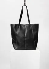 Bolso tipo tote bag negro con textura símil cuero y costuras a la vista. Tiene doble asa de hombro, cierre con broche imán y doble bolsillo interior, uno de ellos con cierre.