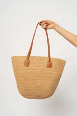 Bolso playero tipo shopper de paja color beige, con asas de cuero marrón.