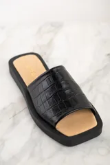 Sandalia abierta negra con textura de cuero de cocodrilo y suela plana.